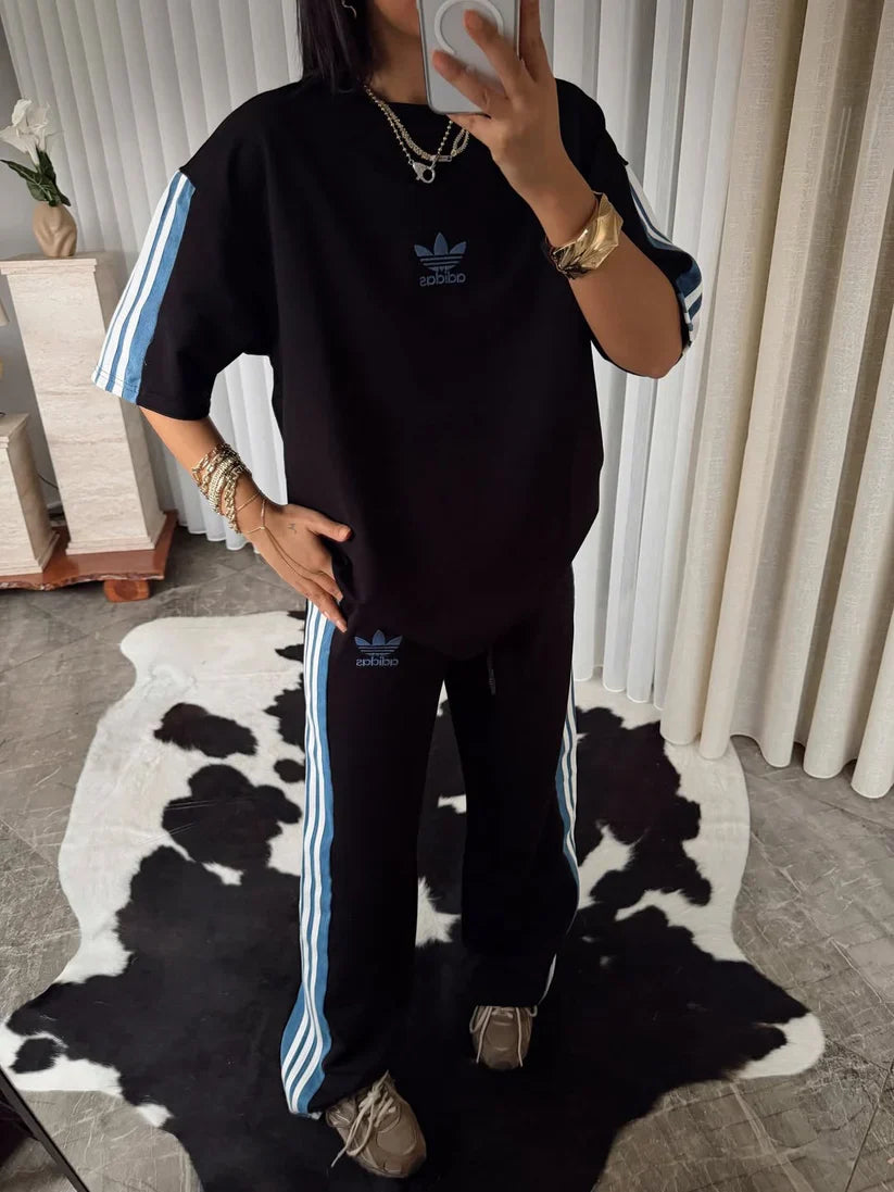 Stylish woman in black oversized co-ord set with striped track pants, sitting indoors and taking a mirror selfie. 03