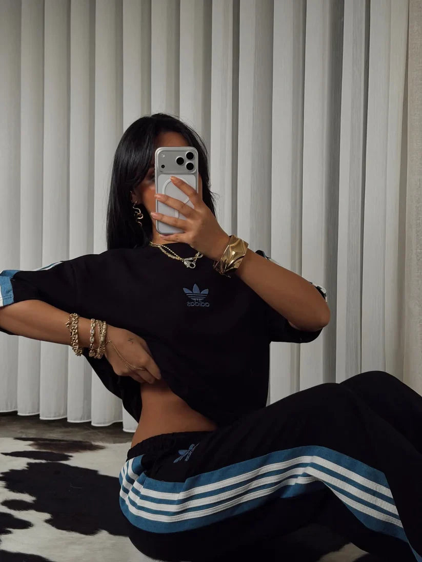 Stylish woman in black oversized co-ord set with striped track pants, sitting indoors and taking a mirror selfie. 04