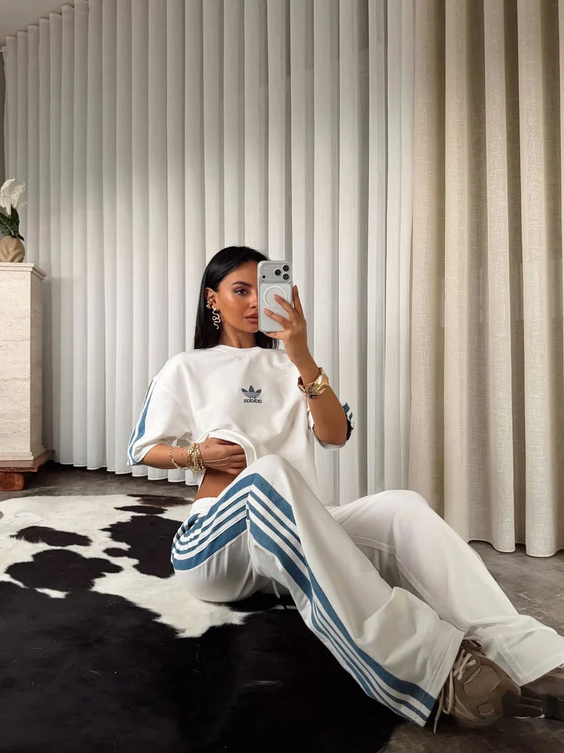 Stylish woman in black oversized co-ord set with striped track pants, sitting indoors and taking a mirror selfie. 05