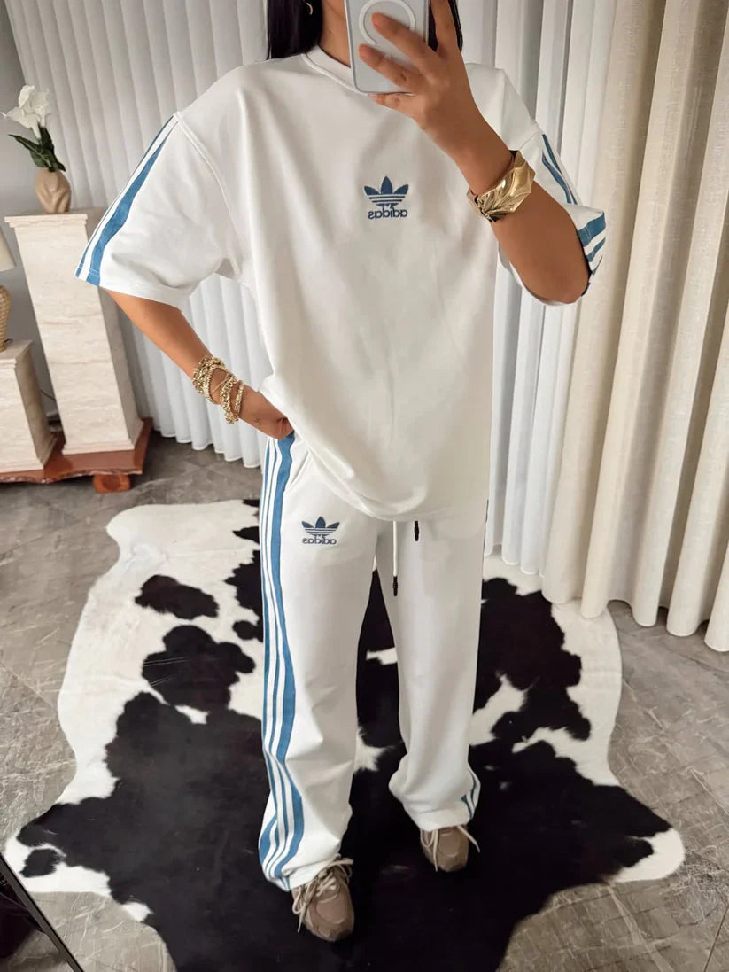 Stylish woman in black oversized co-ord set with striped track pants, sitting indoors and taking a mirror selfie. 07